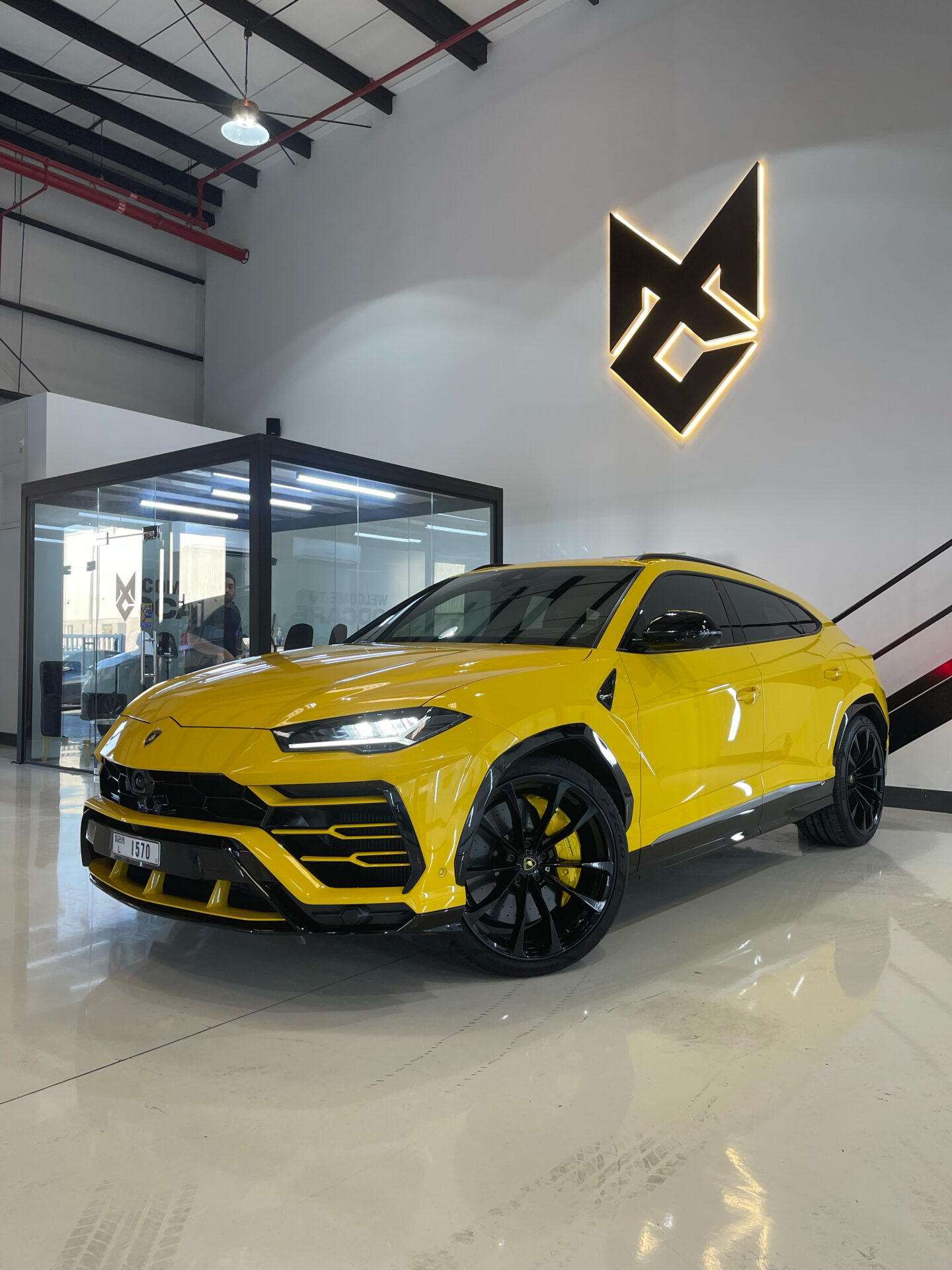A yellow Lamborghini Urus parked in Modcare's Al Quoz studio beneath the illuminated Modcare mark