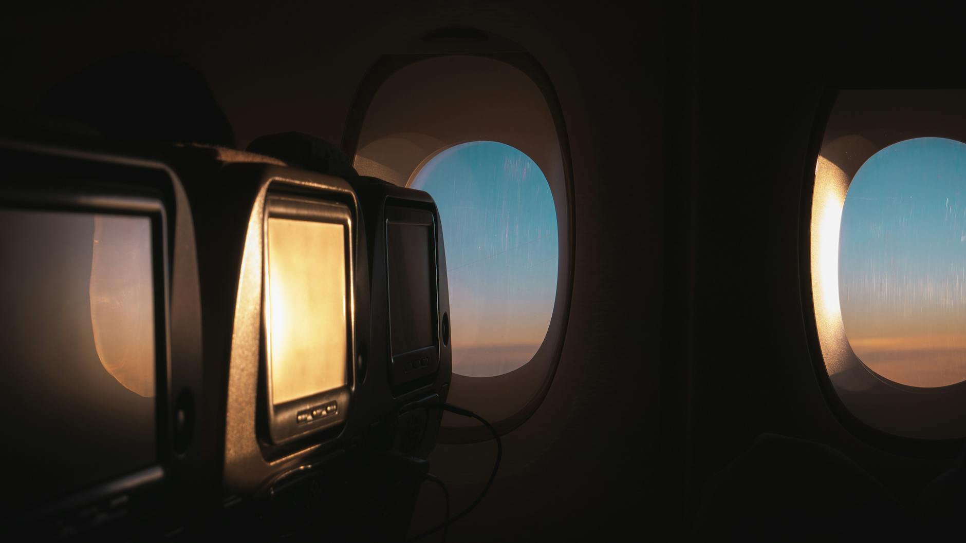 Wide-body cabin window seat with seat-back screens at golden hour